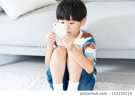 Elementary school boy playing with smartphone in the living room Elementary school boy playing with smartphone in the living room 133230219