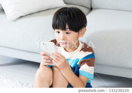 Elementary school boy playing with smartphone in the living room Elementary school boy playing with smartphone in the living room 133230220