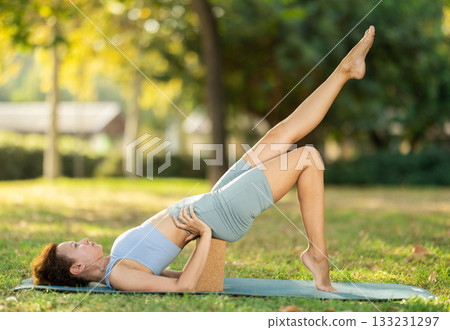 Woman leading an active lifestyle, training in a summer park, performing dynamic asanas to improve body flexibility 133231297