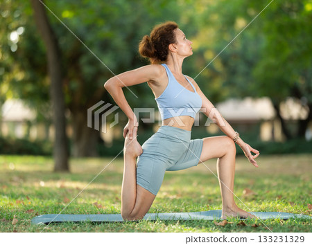 Slim woman practicing yoga - virabhadrasana pose in summer park Slim woman practicing yoga - virabhadrasana pose in summer park 133231329