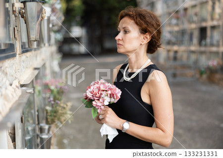 Woman in black dress with bouquet of flowers came to cemetery to honor the memory of deceased loved one 133231331