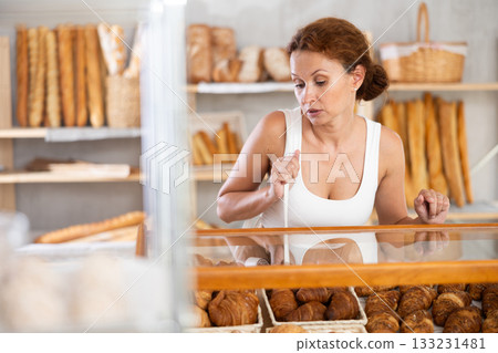 Woman in casual clothes chooses hot croissants for breakfast in bakery Woman in casual clothes chooses hot croissants for breakfast in bakery 133231481