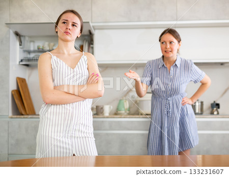 Offended young girl standing in the kitchen, angry mother talking 133231607
