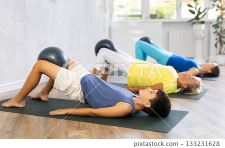 Mom, grandmother and teen grandson performing exercises with softball lying on floor 133231628
