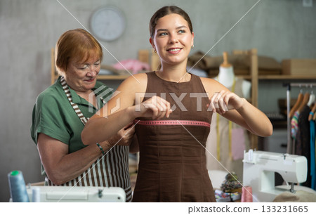 Elderly seamstress takes body measurements from young woman 133231665