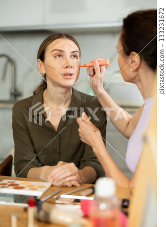Woman doing contour makeup to relaxed female friend at home 133231672