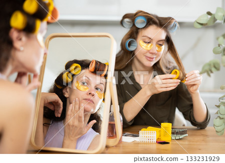 Two women curl their hair with curlers and use patches 133231929