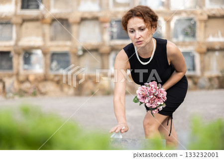 Woman in black laying bouquet on grave in cemetery 133232001