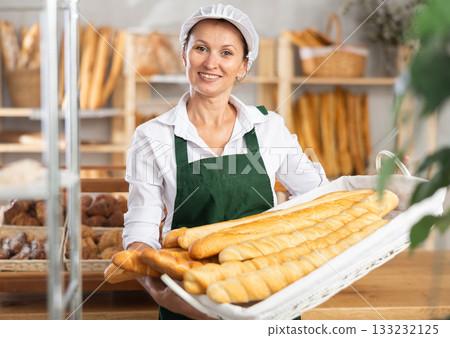 Female baker worker sells baguette, shows many products 133232125