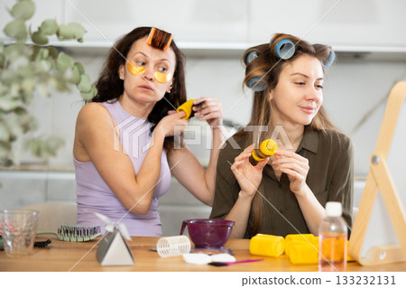 Relaxed women curling hair with colorful rollers at home 133232131