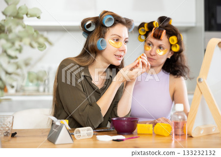 Female friends in colorful rollers applying golden under-eye patches Female friends in colorful rollers applying golden under-eye patches 133232132