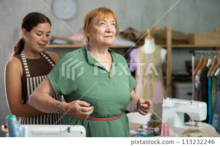 Young seamstress takes body measurements from elderly woman 133232246