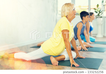Mother, grandmother and teen son do exercise dove pose, Eka Pada Rajakapotasana. Mother, grandmother and teen son do exercise dove pose, Eka Pada Rajakapotasana. 133232256