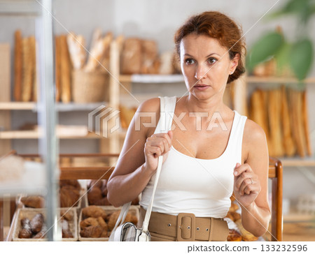 Young European woman near window of bakery food court store examines assortment 133232596