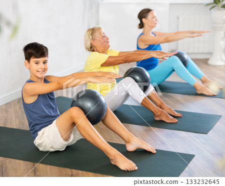 Preteen boy practicing fitness with softball between legs in light training room Preteen boy practicing fitness with softball between legs in light training room 133232645