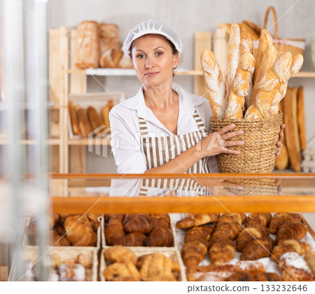 Female baker worker sells baguette, shows many products 133232646