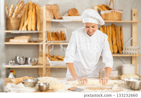 Process of making baguette, loaf or bread in bakery - female baker kneads and rolls dough to give shape of future bread 133232660