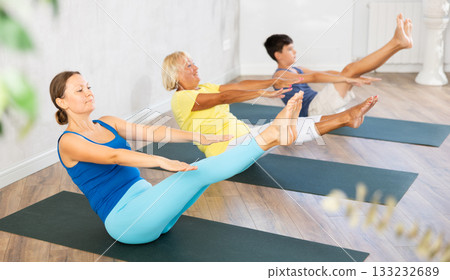 Grandmother, mother and teen son do sitting boat pose Paripurna Navasana in gym Grandmother, mother and teen son do sitting boat pose Paripurna Navasana in gym 133232689
