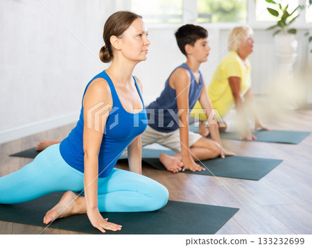 Mother, grandmother and teen son do exercise dove pose, Eka Pada Rajakapotasana. 133232699