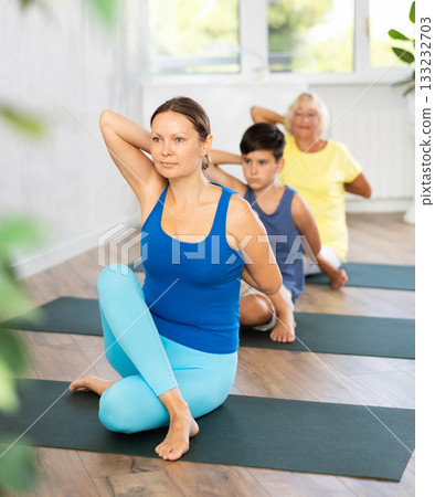 Middle-aged woman practicing cow face pose of yoga in light fitness room Middle-aged woman practicing cow face pose of yoga in light fitness room 133232703