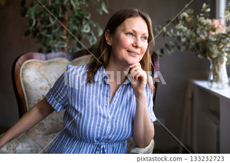 Girl is sitting in semi-dark room among indoor plants of ficus trees and remembers plot of book 133232723