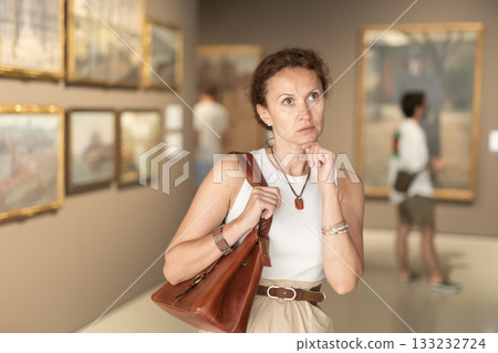 Portrait of attentive woman looking at pictures and amaze in art museum Portrait of attentive woman looking at pictures and amaze in art museum 133232724