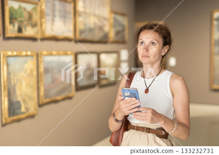 Pretty young woman with phone in hands looking at medieval expositions in museum 133232731