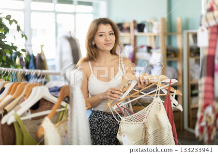 Young woman chooses dresses and tops in store Young woman chooses dresses and tops in store 133233941