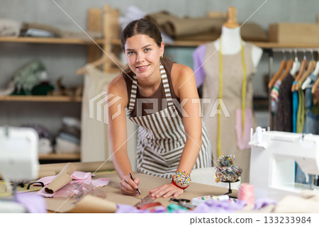 Female fashion designer drawing on paper with curved rulers in workshop 133233984