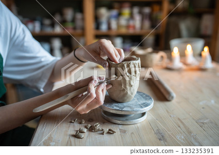 Potter hands shaping mug with loop tool, carve intricate pattern, scraping excess clay. Artisan job Potter hands shaping mug with loop tool, carve intricate pattern, scraping excess clay. Artisan job 133235391