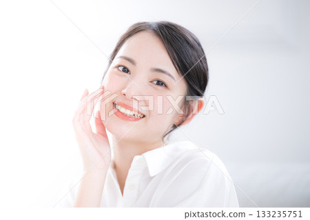 A clean-cut young woman in a white shirt smiles and shows skin care and beauty. Close-up, looking at the camera. A clean-cut young woman in a white shirt smiles and shows skin care and beauty. Close-up, looking at the camera. 133235751