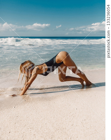Woman in swimwear stretching on a sunny beach with waves and blue sky Woman in swimwear stretching on a sunny beach with waves and blue sky 133236054