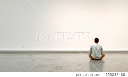 Man sitting alone on floor facing empty white wall, contemplative and calm in modern interior Man sitting alone on floor facing empty white wall, contemplative and calm in modern interior 133236488