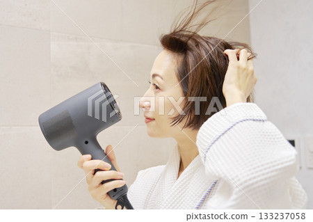 婦女用吹風機烘乾她的頭髮。 133237058