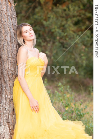 An Elegant Woman Wearing a Beautiful and Stylish Yellow Dress Poses Gracefully by the Tree An Elegant Woman Wearing a Beautiful and Stylish Yellow Dress Poses Gracefully by the Tree 133237481
