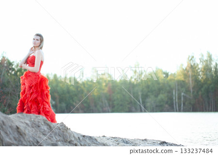 An Elegant Model Dressed in a Fiery Red Dress Posing Gracefully by the Waters Edge An Elegant Model Dressed in a Fiery Red Dress Posing Gracefully by the Waters Edge 133237484
