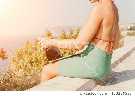 Woman Laptop Beach - Working remotely on a laptop by the ocean during sunset. 133238553