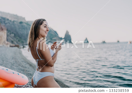 Woman, beach, phone, smiling woman texting on smartphone by ocean cliffs during summer vacation. Woman, beach, phone, smiling woman texting on smartphone by ocean cliffs during summer vacation. 133238559