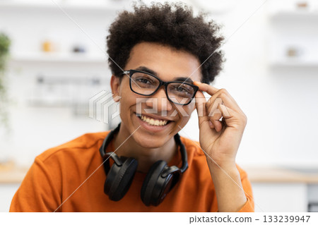 A young man with glasses smiles directly at the camera, with headphones around his neck. A young man with glasses smiles directly at the camera, with headphones around his neck. 133239947