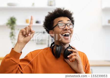 A young man with glasses points upwards, looking excited with headphones around his neck. A young man with glasses points upwards, looking excited with headphones around his neck. 133239953