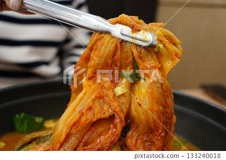 Tongs Lifting Spicy Korean Aged Kimchi from a Hot Pot 133240018