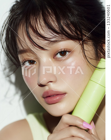 一位美麗的亞洲模特兒一手拿著一瓶潤膚露，直視鏡頭。 133240601