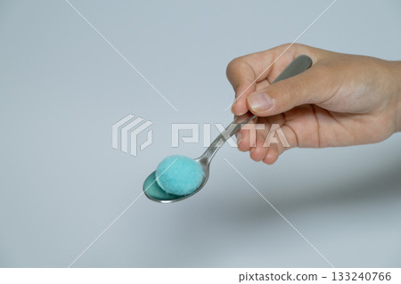 A hand holding a spoon with blue cotton balls on it A hand holding a spoon with blue cotton balls on it 133240766