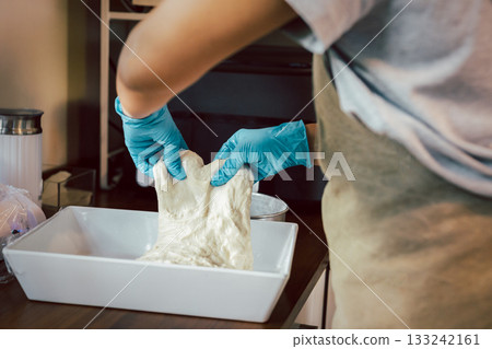 Woman hand with glove preparing bread dough on wooden table. 133242161