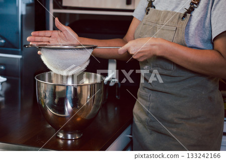 Woman sifting the flour into a metal bowl for making dough. 133242166