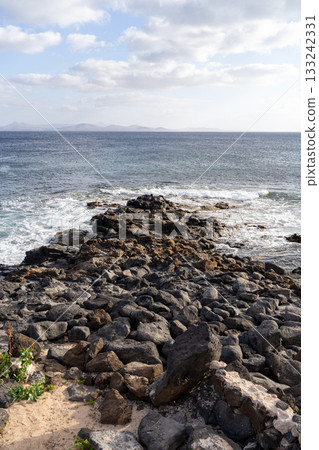 The rocky coastline of Lanzarote meets the Atlantic ocean under a partly cloudy sky on a beautiful day.  133242331