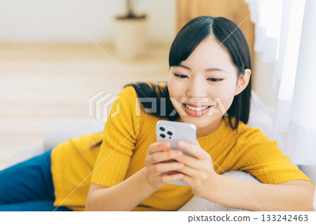A young lady watching a smartphone on a sofa A young lady watching a smartphone on a sofa 133242463