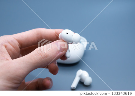 Hand Removing White Earbud from Case 133243619