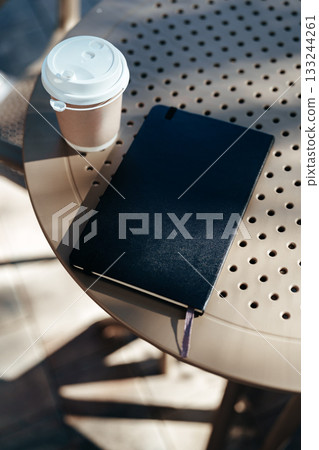 Coffee and notebook on a round table in a sunny outdoor cafe setting Coffee and notebook on a round table in a sunny outdoor cafe setting 133244261