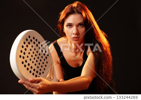 Woman in black dress poses dramatically with circular object in low light setting 133244269